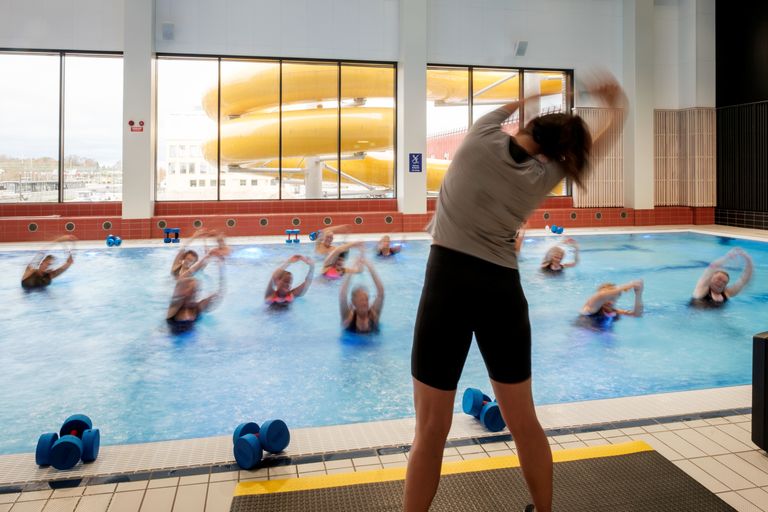 Bild på personal som står vid poolkanten och håller i ett pass för kvinnor som tränar i vattnet