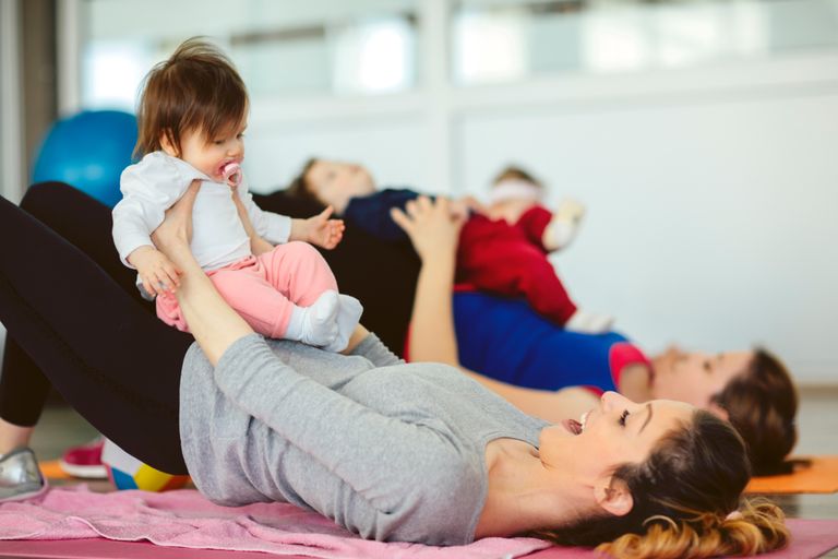 Bild på en mamma som ligger på en yogamatta med sin bebis i knät