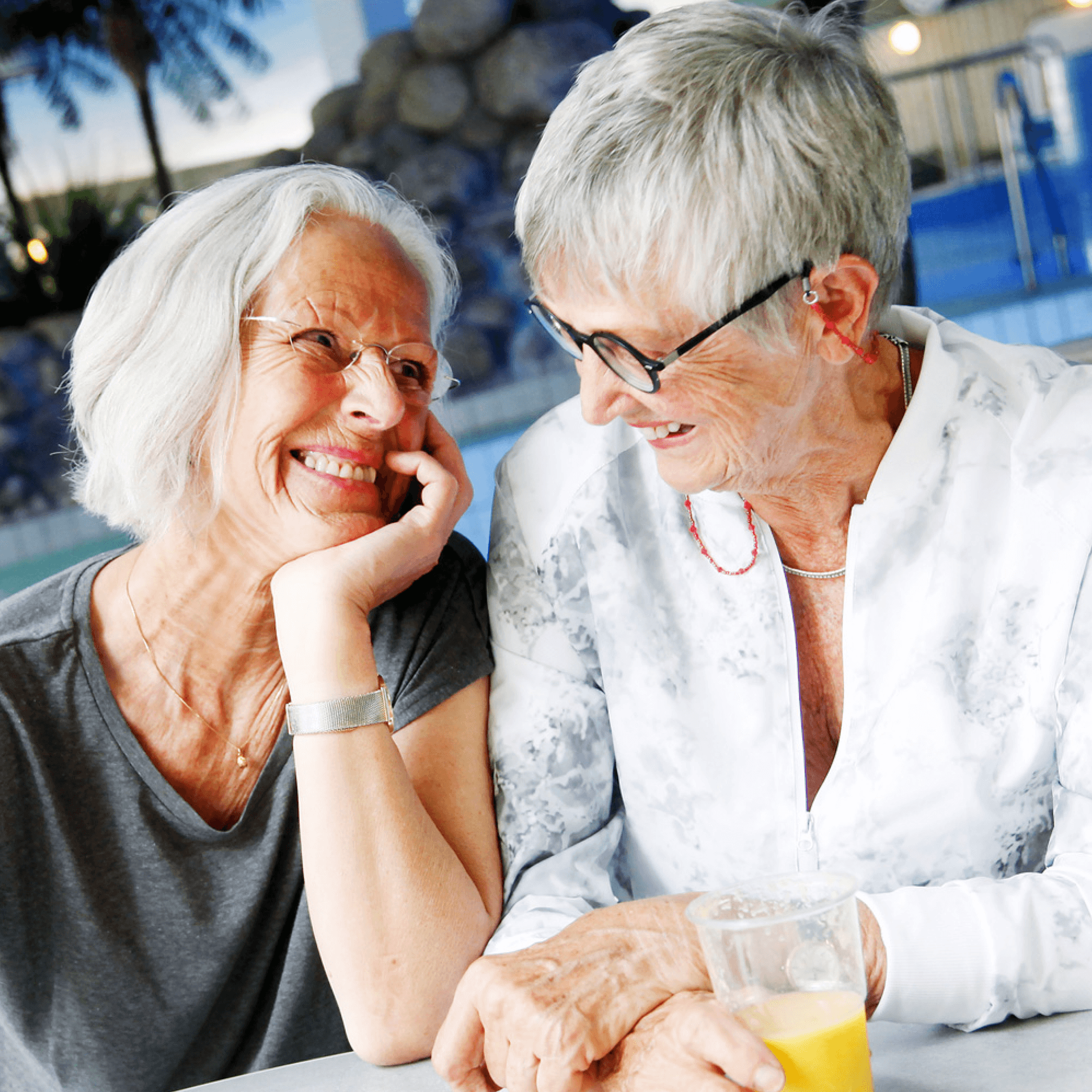 Bild på två äldre kvinnor sitter vi ett bord och skrattar medans dom fikar i simhallen
