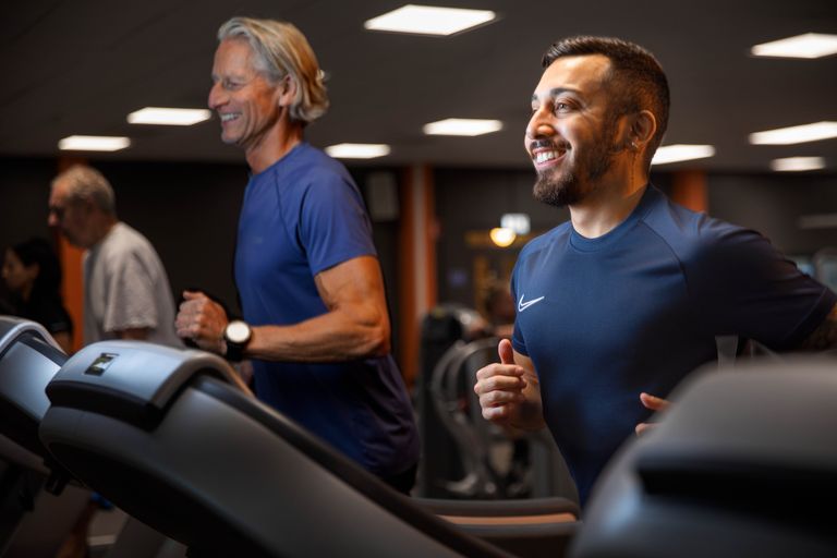 Två personer står på varsitt löpband i ett gym. De ler och springer medan de tittar framåt.
