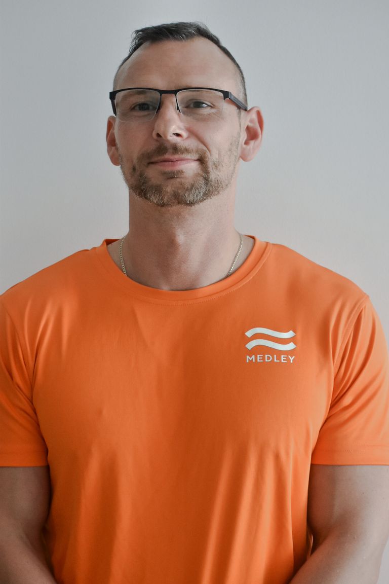 En man med glasögon och en orange t-shirt med Medley-logotypen.