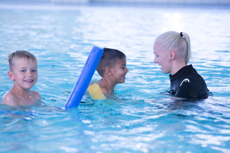Bild på barn som får hjälp att simma av en instruktör.