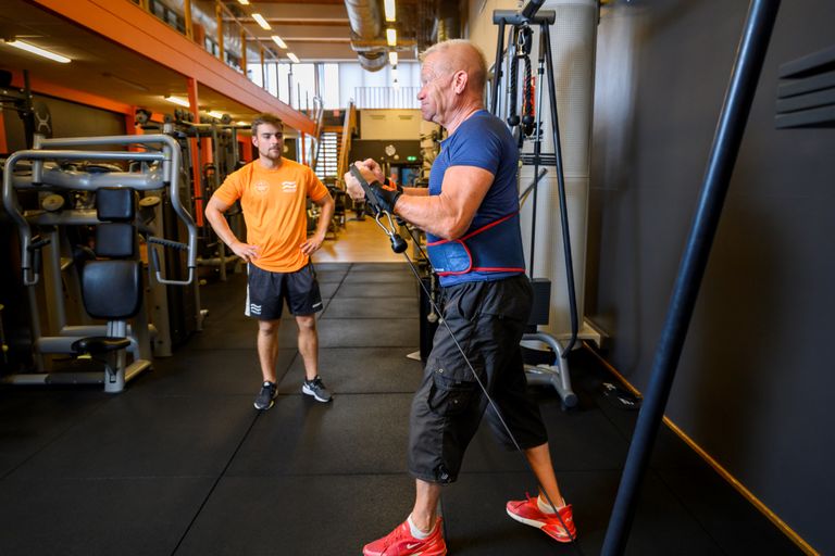 Bild på en man som kör bröst i gymmet medans hans PT tittar på och peppar