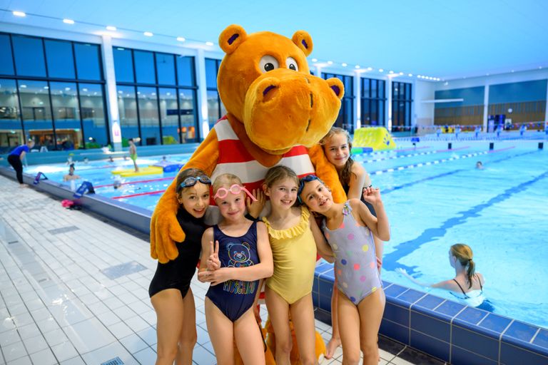 Bild på Flodis och fem barn som står framför en pool.