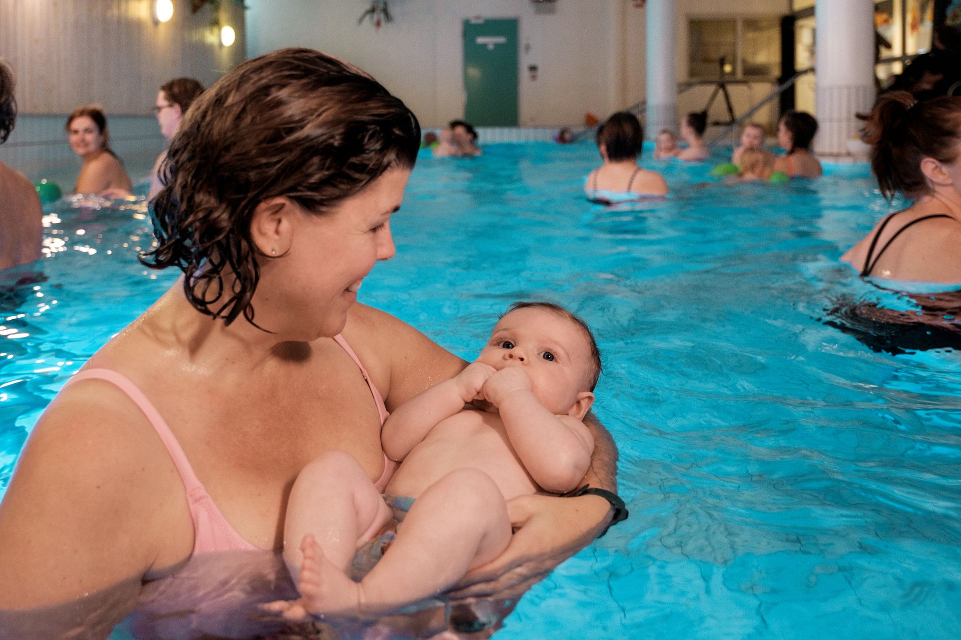 Bild på mamma i vattnet som håller sin bebis i famnen i bassängen