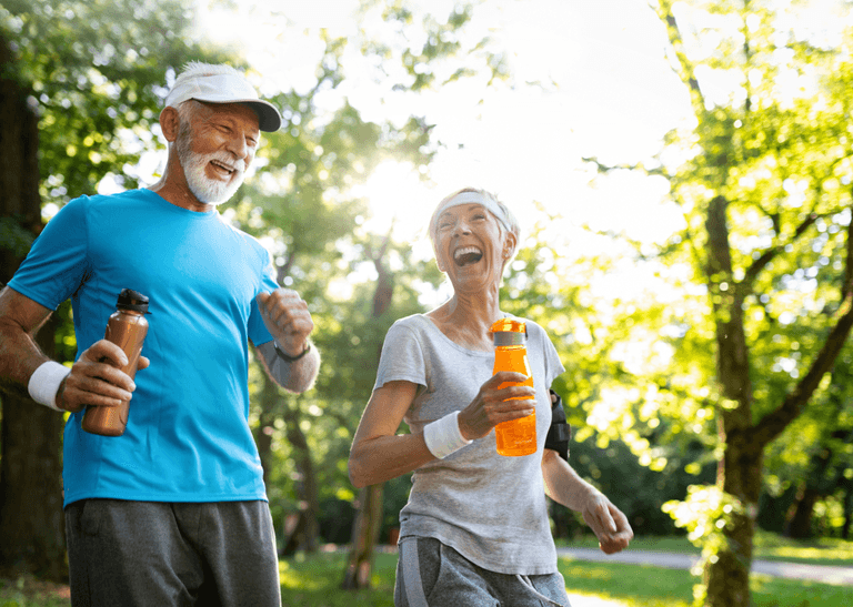 Två äldre personer är ute på springtur i en park en solig sommarmorgon. Mannen är klädd i ljusblå tshirt och kvinnan i en vit tshirt. I sina händer håller de varsin vattenflaska.