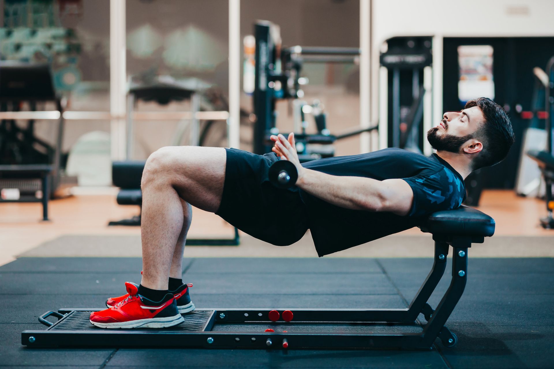 Man i gymmet ligger med ryggen mot en bänk och gör hip trusters med vikte lutat mot höften samtidigt som han lyfter höften mot taket. 