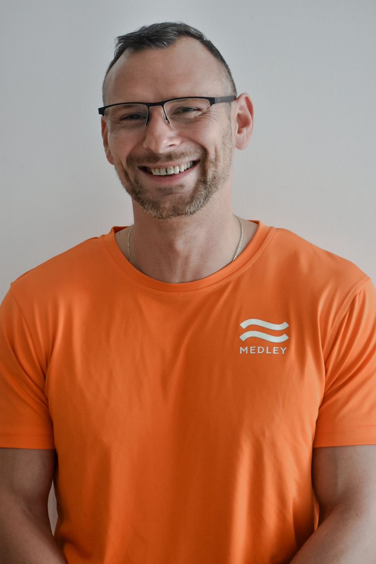 En leende man med glasögon och en orange t-shirt med ett Medley-märke.