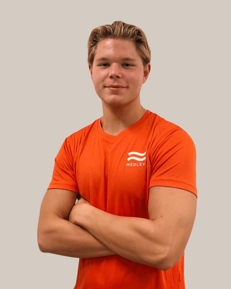 En ung man med blont hår som bär en orange t-shirt med Medley-logotypen och står med armarna i kors.