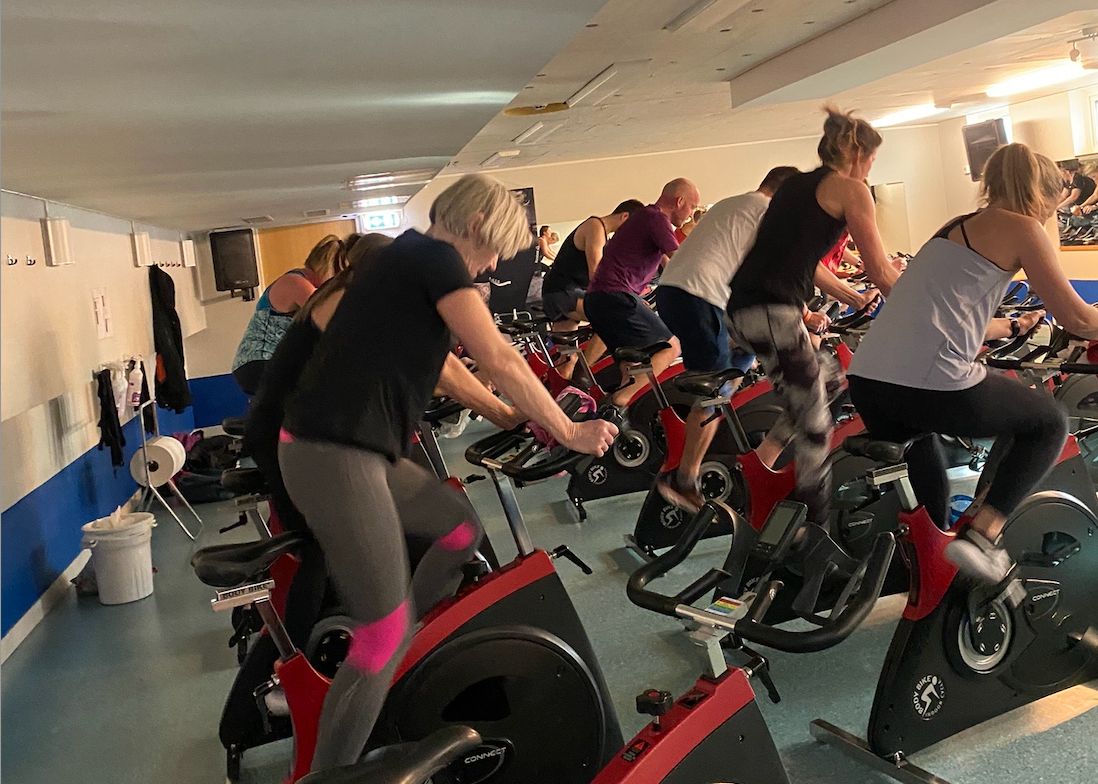 Bild på flera personer under ett spinningpass på röda och svarta cyklar