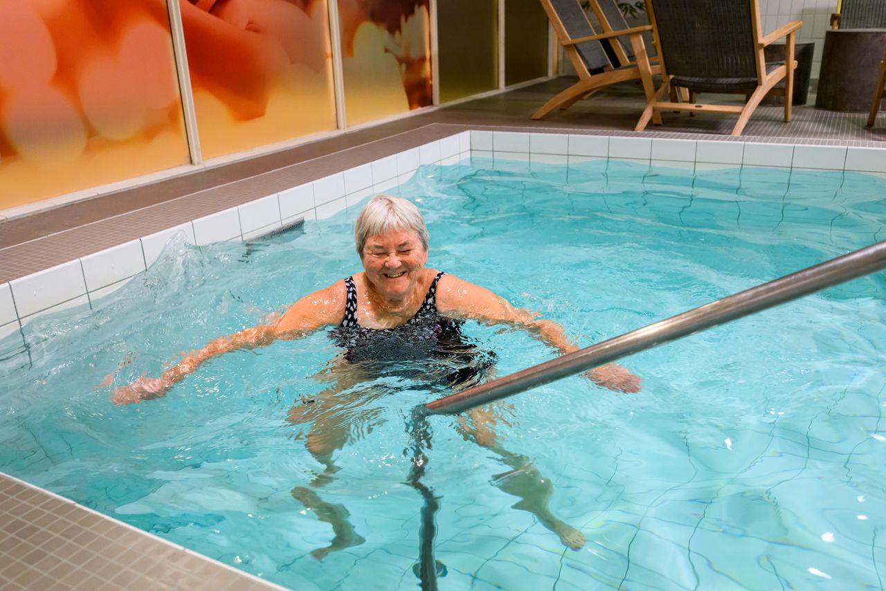 Bild på en glad kvinna i baddräkt som står i en bassäng i relaxen