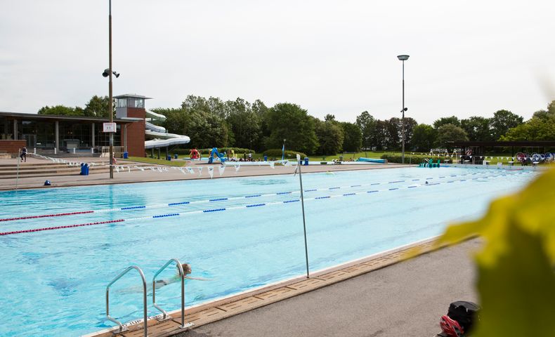 Bild på Centralbadets utomhuspool. En pojke simmar och man ser en vattenrutschkana i bakgrunden.