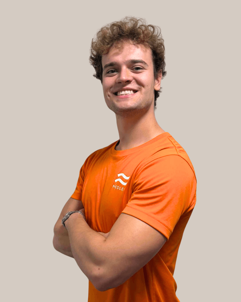 En leende ung man med lockigt brunt hår, klädd i en orange t-shirt med ett Medley-märke.