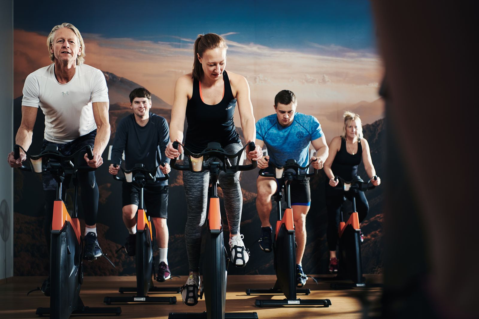 En grupp personer deltar i ett spinning-pass och sitter på varsin cykel i en gruppträningslokal inomhus.