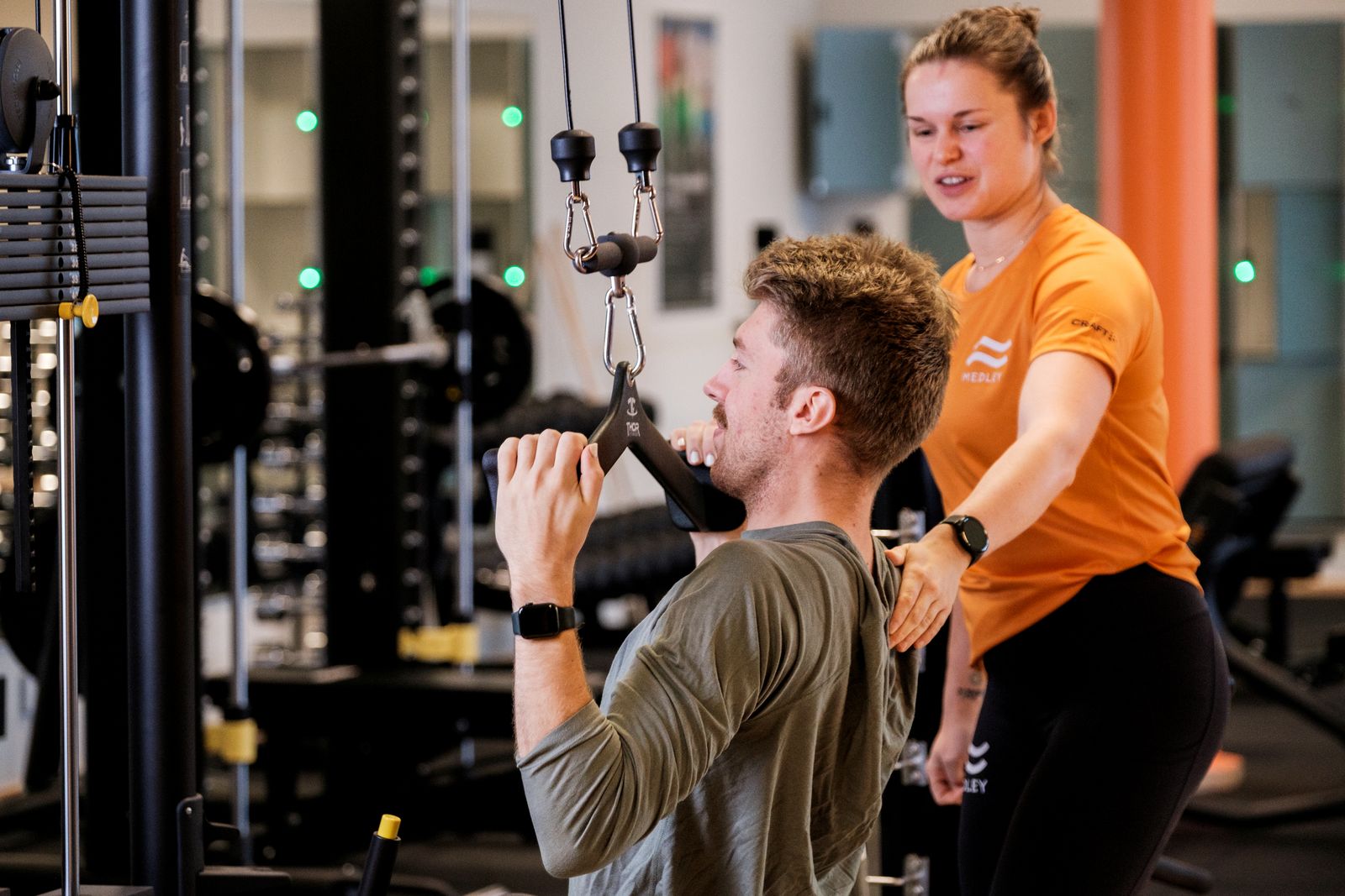 Bild på en pt som instruerar en kille som gör axelpress i maskin