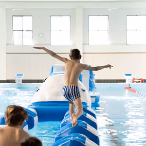 Ett barn balanserar på en uppblåsbar hinderbana i en inomhuspool.