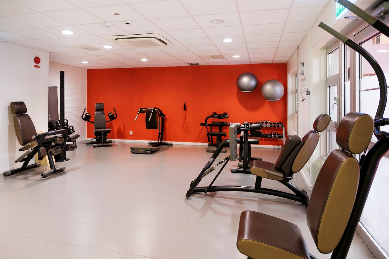 Bild på ett rött rum men träningsmaskiner längssidorna och silvriga pilatesbollar på väggen