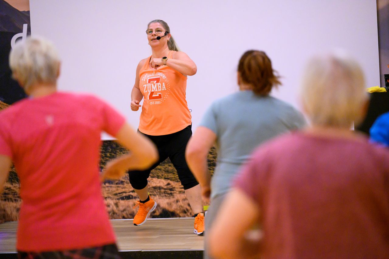 Bild på kvinna i orange t-shrt som instruerar ett gruppträningspass